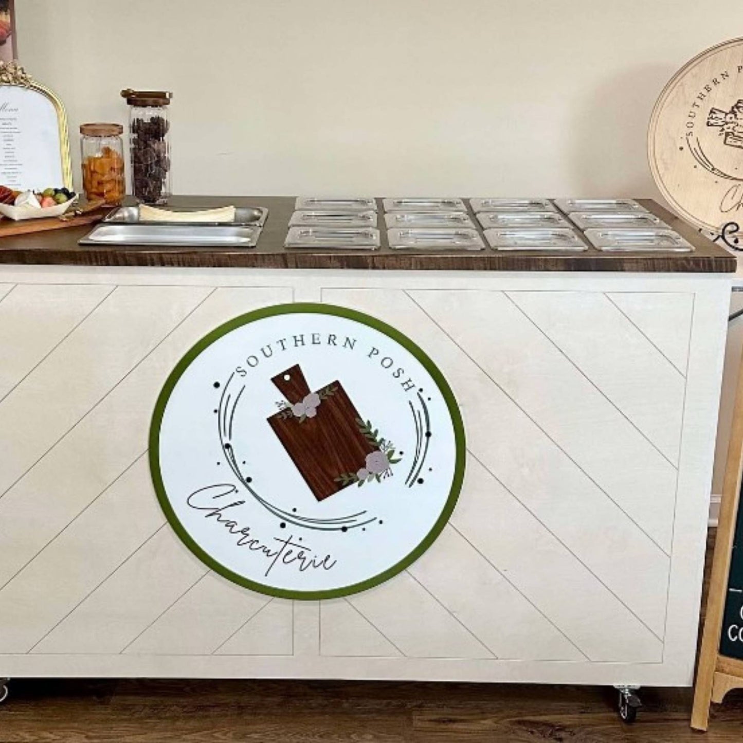 white round business sign bordered with green and layered with their logo attached to a charcuterie cart