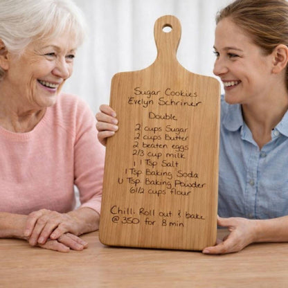 mother and daughter at kitchen table with a recipe board engraved with the mother's cookie recipe in her handwriting